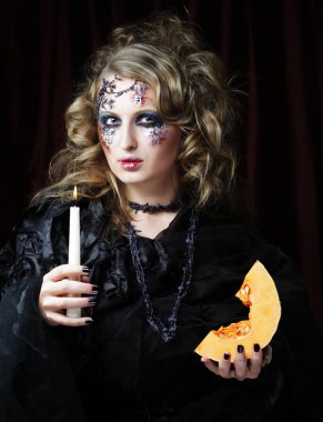 Cadı kostümlü, parlak makyajlı ve elinde Cadılar Bayramı sembolü olan bir balkabağı tutan genç ve güzel bir kadın. Parti zamanı. Tatil günü. Karnaval.