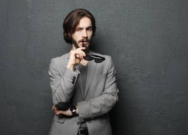 Gri arka planda güneş gözlüğü takan genç yakışıklı bir adamın portresi. Stüdyo moda portresi.
