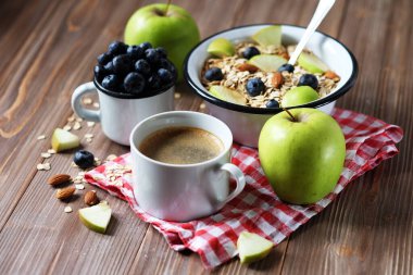 Sağlıklı bir kahvaltı yeni bir güne harika bir başlangıçtır. Tahta bir masada yulaf lapası, kahve, elma, böğürtlen ve fındık..