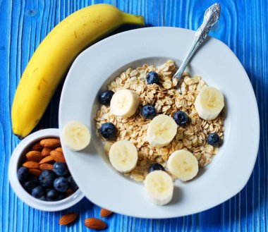 Sağlıklı kahvaltı, yemek ve diyet konsepti - taze dutlu yulaf ezmesi, portakal suyu ve sütle beyaz tabakta muzlar, mavi ahşap arka plan.