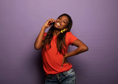 Çekici, sevimli, neşeli, neşeli, mutlu afro kadının portresi. Akıllı telefonu tutan ve parlak mor arka planda izole edilmiş harika haberleri duyan afro kadın.