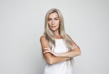 Gri arka planda kolları bağlı yaşlı bir kadın ayakta duruyor. Yaşlı, son sınıf öğrencisi, 60 'lı yaşlarda, beyaz saçlı, kollarını kavuşturup, portreye yakın duran bir kadın..