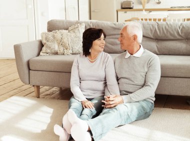 Yaşlı bir çift oturma odasının zemininde otururken sarılıyor. Sarılma, aşk, şefkat. İlişki ve aile kavramı.