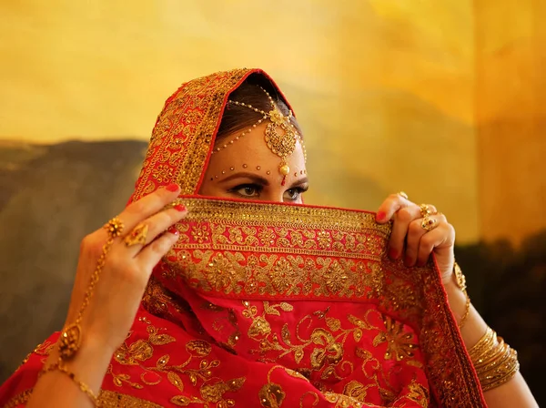 Beautiful indian female. Young hindu woman model with jewelry. Traditional Indian costume red saree. Indian or Muslim woman covers her face.