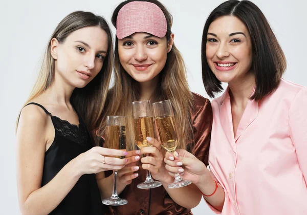 Three young happy women dressed in pajamas drink champagne and have fun, pajama party and friendship concept.