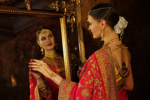 女模特儿 穿着萨里的印度教新娘 头发上戴着黄金和茉莉花环 照镜子 摸着自己的倒影 回头看 — 图库照片