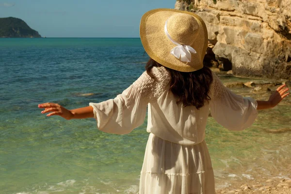 海を見てわら帽子と白い夏のドレスで若いブルネットの女性 バックビューでは 女性は海を賞賛 — ストック写真
