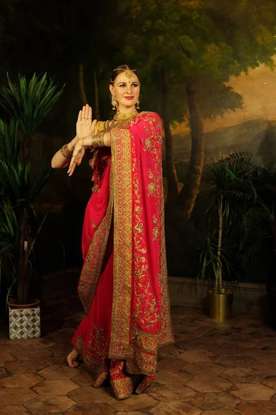 A young beautiful woman in a red sari, a traditional Indian bride, dances and smiles.