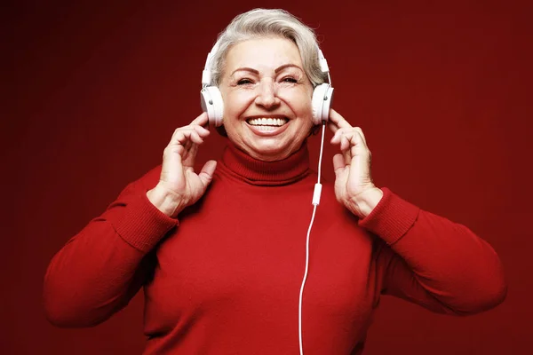 Lifestyle, party, emotion and old people concept: elderly woman wearing red sweater listening to music with headphones