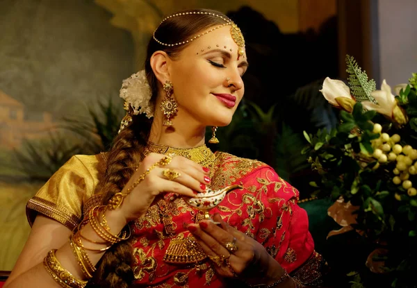 迷人的印度新娘 身穿印度教红色传统婚纱 绣有黄金 坐在花边的沙发上 微笑着 手持小金盒 — 图库照片