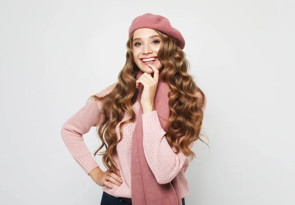 笑顔のブロンドの女性モデルは カメラを見て 若いです巻き毛を身に着けていますピンクのセーター スカーフ そしてグレーの背景にベレー帽 — ストック写真