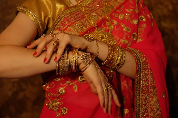 Hands of an indian bride close-up. Lots of jewelry, traditional red sari.
