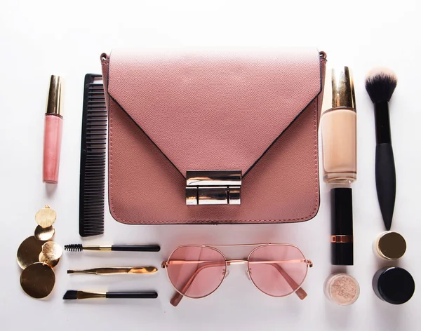 Flat lay of pink leather bag with cosmetics and accessories , white background.
