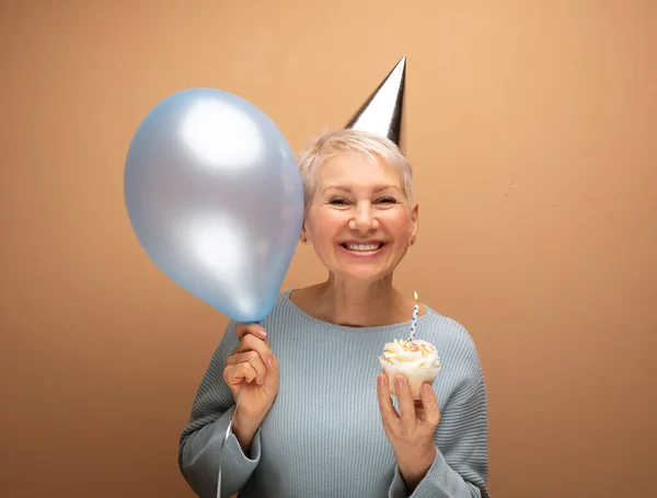 衰老和成熟的概念 漂亮的老妇人戴着圆锥形的帽子庆祝生日 手里拿着蜡烛和蓝色气球摆出孤零零的架势 快乐时光 — 图库照片