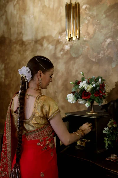 A young woman in a traditional Indian wedding dress opens drawers in a chest of drawers while standing with her back to the camera. Lifestyle concept.