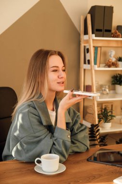 Güzel genç bir kadın akıllı telefondan sesli mesaj kaydediyor. İş kadını evde otururken sanal asistan uygulaması kullanıyor. Ses tanıma, sesli mesajlar, cep telefonunda çevirmen kullanımı.