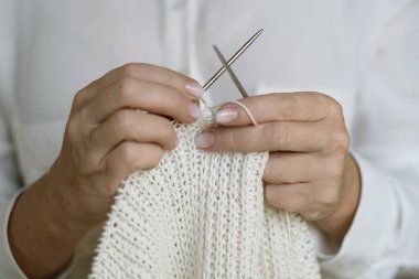Woman's hands knitting white wool yarn pattern. Closeup horizontal photo.