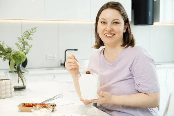 Pretty Plump Woman Sits Kitchen Eats Noodles Paper White Box — Zdjęcie stockowe