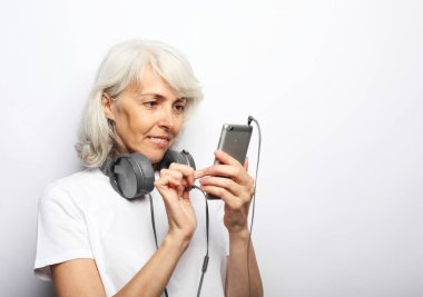 Kulaklıklı yaşlı bir kadın elinde cep telefonuyla ekranı kaydırıyor, şarkı seçiyor. Yaşam tarzı ve insan kavramı.