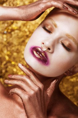 Parlak, pürüzsüz, sağlıklı bir cilde sahip genç bir kadının portresi belirgin boyanmış gözler ve dudaklarda altın. Altın arkaplan.
