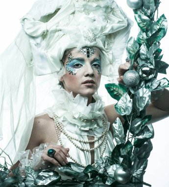 Parti, Noel ve insanlar: Noel karnavalı için kostüm giymiş güzel bir kadın Noel süslemeleri ve gümüş yapraklar çerçevesinde poz veriyor. Yaratıcı makyaj, saç stili.