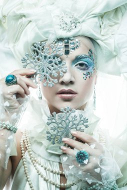 Parti, noel ve halk konsepti: Yeni yıl kostümlü güzel bir kadın gözlerini gümüş kar taneleriyle kapatır. Peri, büyücü, peri masalı karakteri.