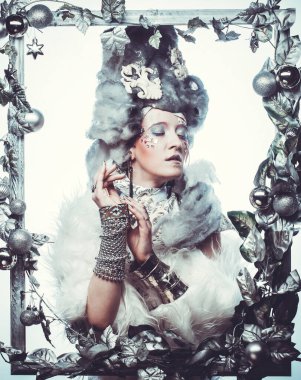 Parti, Noel ve halk konsepti: Gümüş sanatsal makyajlı, peruklu, Noel süslemeleri ile süslenmiş gümüş çerçevede poz veren yaratıcı görünümlü genç kadın. Kış Portresi. Kar Kraliçesi.