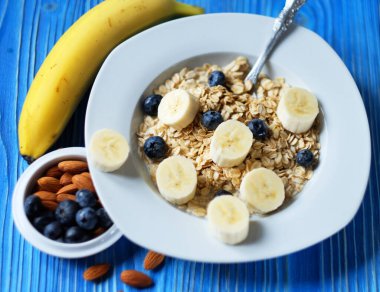 Sağlıklı kahvaltı, yemek ve diyet konsepti - taze dutlu yulaf ezmesi, portakal suyu ve sütle beyaz tabakta muzlar, mavi ahşap arka plan.