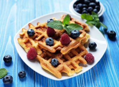 Good morning. Waffles with blueberries and raspberries for breakfast over blue wooden table.