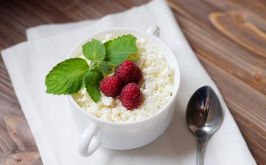 Good breakfast. Cottage cheese with mint and raspberries in a white bowl over wooden baclground.