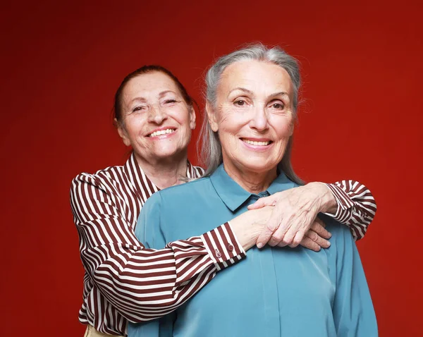 两个老年女性朋友依偎在红色的背景上 生活方式 友谊和老年人概念 — 图库照片