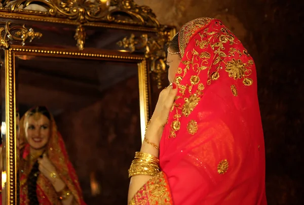 一位穿着红色萨里的漂亮女人 传统的印第安婚纱 新娘对着镜子 欣赏着自己的倒影 头戴头巾的女人 印度文化 — 图库照片