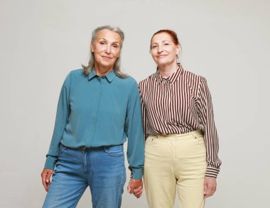 Two pretty elderly women friends on grey background. Lifestyle concept.