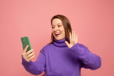 It's selfie time. Image of cheerful woman standing isolated over pink background wall talking by mobile phone.