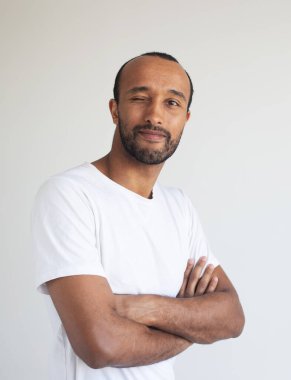 A young unshaven man with crossed arms on a light gray background. African American. Close-up portrait.