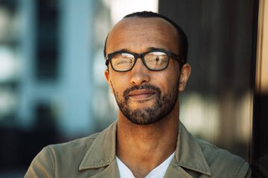 A young unshaven afro american smiling man wearing eyeglasses on the street. Outdoor portrait. Close up.