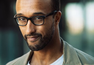 A young unshaven afro american smiling man wearing eyeglasses on the street. Outdoor portrait. Close up.