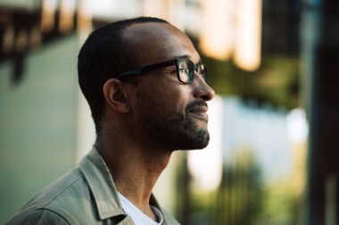 A young unshaven afro american smiling man wearing eyeglasses on the street. Outdoor portrait. Close up.