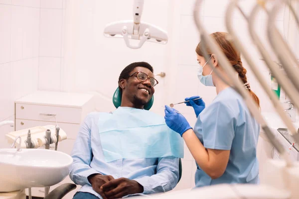 People, medicine, stomatology, technology and health care concept. A young woman dentist checks the teeth of a black man.