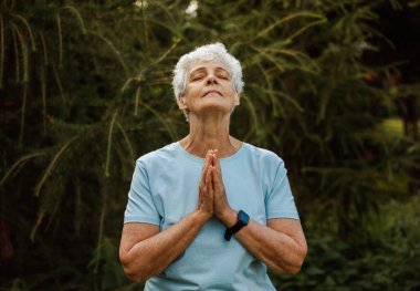 Elderly woman with short hair practicing yoga and tai chi outdoors. Old female meditating. Senior woman is doing yoga in the park. Smiling aged lady exercising.