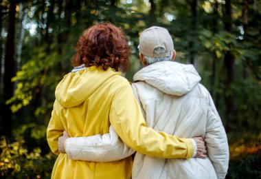 Two old female friends hiking together through the forest in autumn. Back view. Lifestyle and friendship concept.