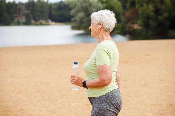 Elderly Happy Retired Woman Jogging Old Woman Runs Beach Holds — Zdjęcie stockowe