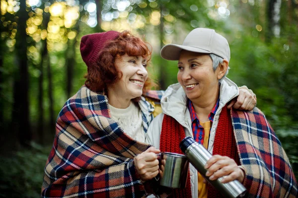 2つの高齢者の女性の友人が森の中を歩くと 魔法瓶からコーヒーを注ぐ 一緒に素晴らしい時間を過ごす 高齢者の幸せなカップル — ストック写真