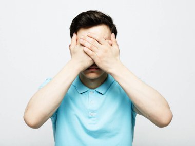 young handsome man covers his eyes with his palm over grey background