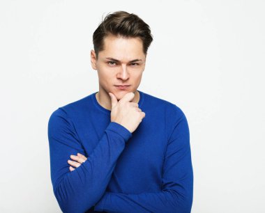 a young man in a blue sweater touches his chin thoughtfully, thinking about something, portrait over white background