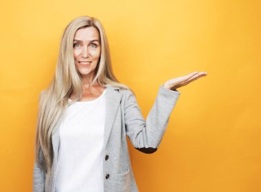 Smile elderly woman wearing casual holding something on open palm over yellow background.
