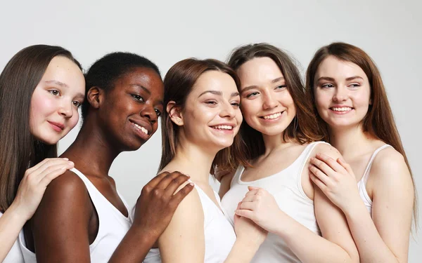 Group of five young female friends of different nationalities over grey background
