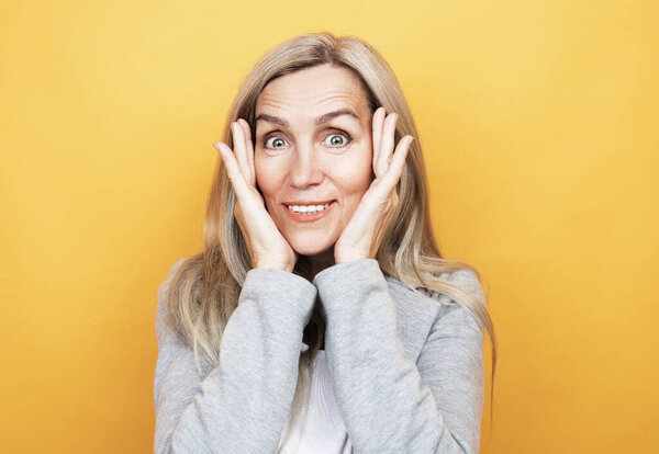 lifestyle, emotion and people concept: old nice beautiful surprised woman with ling hair. Isolated over yellow color background.