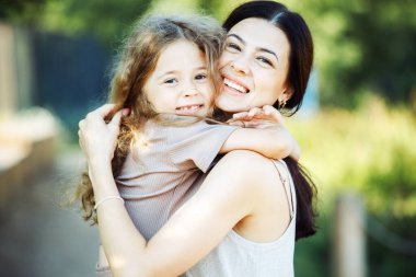 Happy summer time. Little daughter hugging her young happy mom in the park.