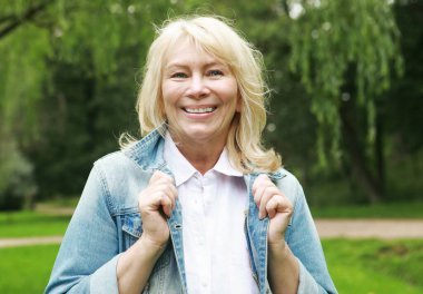 Beautiful blonde woman in a denim jacket in a spring park. Elderly happy lady pensioner. Close up. Golden age.
